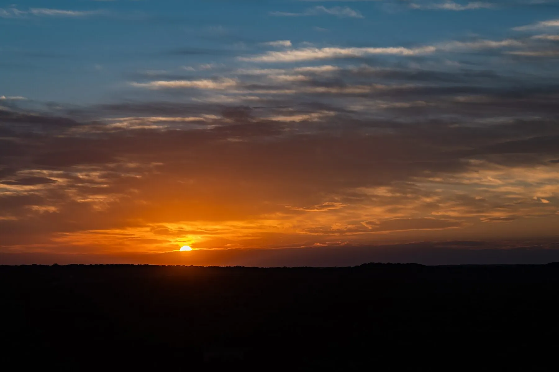 Orange sunset beneath layered clouds at Pedernales Falls State Park
