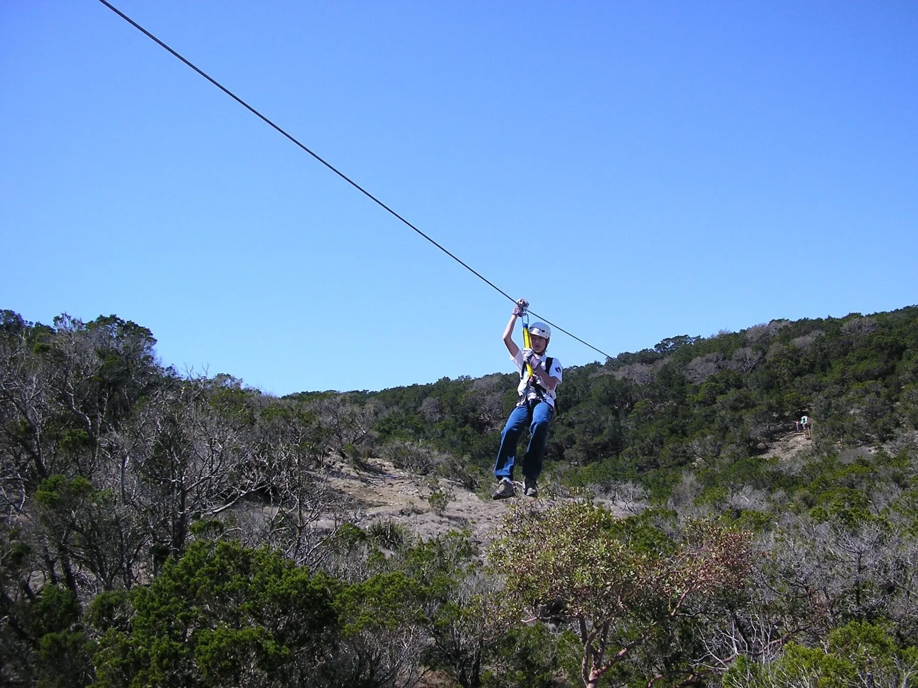 A rider travels along a zip line above trees at Wimberley Zipline Adventures
